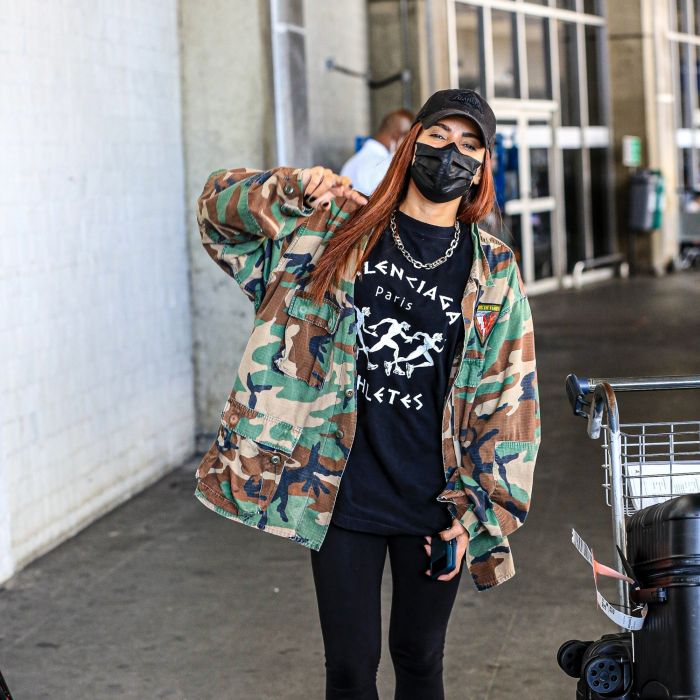 Anitta combina look all black com maxi casaco com estampa militar em aeroporto