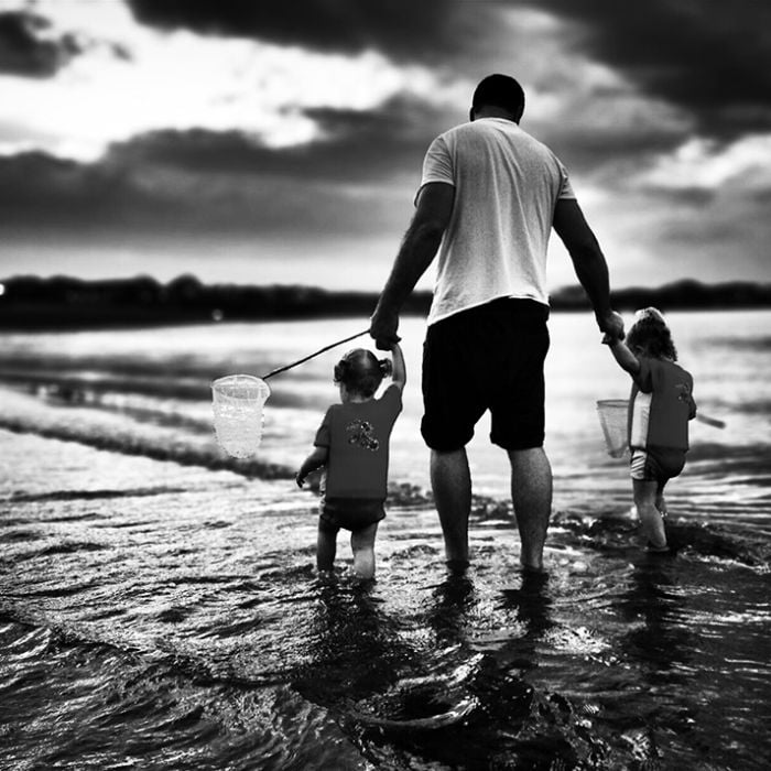 Belo registro de um pai caminhando com suas filhas na beira de uma praia da África do Sul.